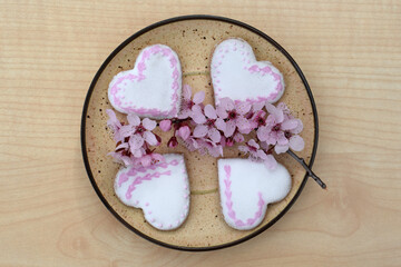 Plate with romantic decorated gingerbread cookies in a shape of hearts, with spring blooming twig