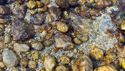 wide view of underwater stones in a shallow river with sun reflections and water movement pattern. natural abstract texture with