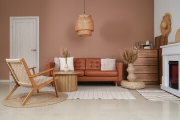Interior of stylish living room with brown sofa, armchair, fireplace and pampas grass