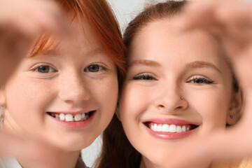 Young ginger woman and her cute daughter taking selfie with heart gesture on grey background