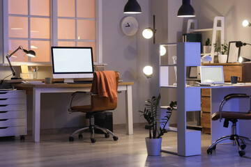 Interior of office with desks and glowing lamps at night
