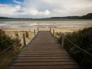 Obraz premium Wooden boardwalk walkway leading to white sand beach at blue turquoise clear freshwater Lake Taharoa Kai Iwi Lakes Northland North Island New Zealand
