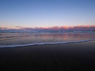 Kaiaua Bay beach spume mirror reflection golden hour sunrise at low tide with glowing colorful clouds near Gisborne North Island New Zealand