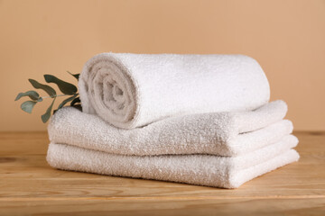 Clean towels and eucalyptus branch on wooden table against color background
