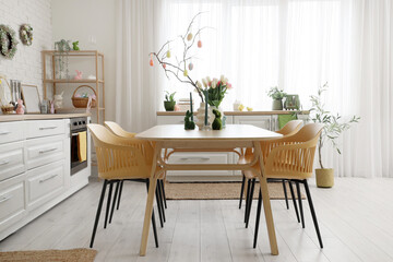 Interior of festive kitchen with tulip flowers, rabbits and Easter painted eggs on tree branches at dining table