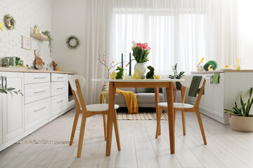 Beautiful flowers with Easter rabbits, baby chickens and candles on dining table in festive kitchen