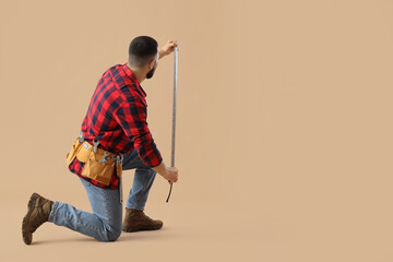 Male construction worker with professional tools and measuring tape on beige background, back view