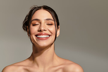 Joyful young woman showcases radiant smile against a neutral background during a bright afternoon