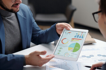 Closeup of businessman holding tablet and presenting data statistics during meeting at table in office copy space