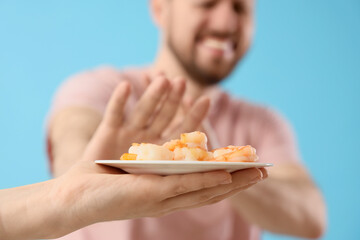 Young man refusing hand with shrimps on blue background, closeup. Food Allergy Awareness Month