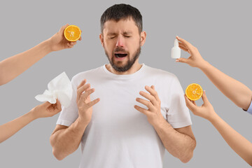 Sneezing young man and female hands holding orange with nasal drops on light background. Food Allergy Awareness Month