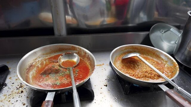 Two metal pans simmering daal mash and chicken salan with rich spices on a stainless steel stove