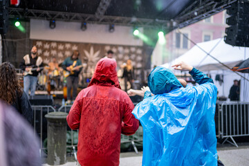 Two persons dancing under the rain in a music festival and concert with waterproof gear blue and red