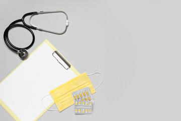 Blank clipboard with stethoscope, pills and protective mask on grey background. World Health Day