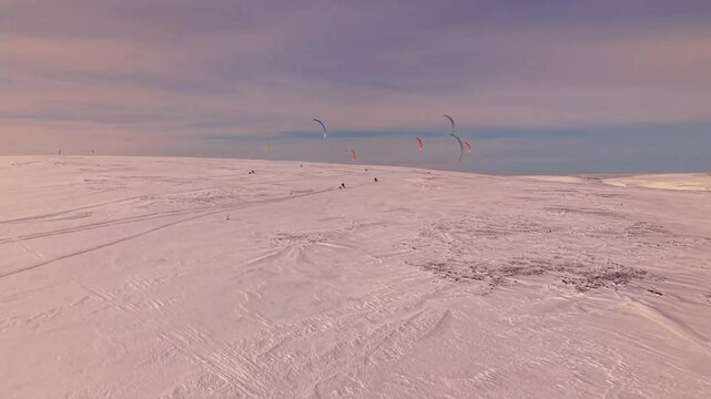 Gorgeous aerial drone footage of people flying and kite skiing with kites on vast large white snow covered Norway landscapes at an endurance race during a winter sunny day.