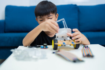 Concentrated Asian student assembling a robotics car using a DIY kit in a vibrant STEM classroom,...