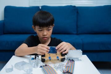 Concentrated asian boy assembling diy robot car at home, educational activities, stem education,...