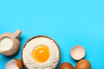Plate with flour, raw eggs and pitcher of milk on color background