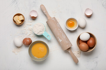 Composition with fresh chicken eggs, flour, butter and rolling pin on light background