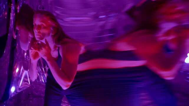 Young woman moving through blurred reflections in distorting mirror surface, creating energetic and surreal contemporary dance performance in multicolored neon illumination