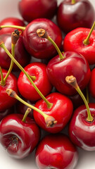 A handful of fresh cherries with stems, placed on a white plate, high contrast