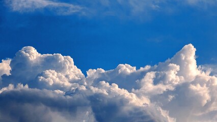 Dramatic view of fluffy white cumulus clouds against a vibrant blue sky. Weather, atmosphere, and natural beauty.