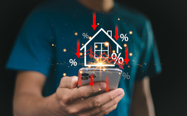 Businessman use smartphone with virtual home icon and down arrow for economical real estate and lower mortgage interest rates. Reduced prices for rental housing, Demand for home purchases decreases.