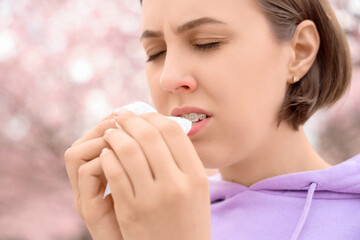 Allergic young woman with tissue sneezing in park, closeup