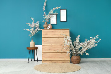 Chest of drawers and vases with blossoming branches near blue wall in room