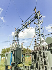 Large industrial electric transformer with high voltage lines against blue sky and clouds. Power substation infrastructure for electricity transmission concept.