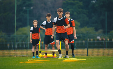 Teen soccer players train on a field, practicing agility drills with yellow hoops and cones. Football summer camp for youth players. Teammates in soccer practice outdoors
