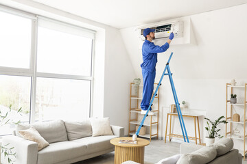 Male technician with screwdriver repairing air conditioner in room