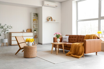 Interior of light living room with brown sofa, armchair and spring flowers in vases