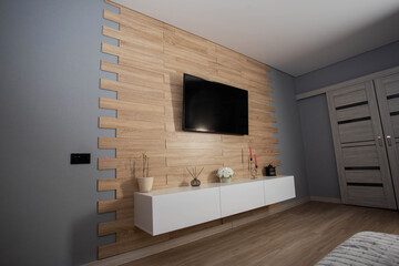 Interior wall with wooden panels against the background of an LCD TV and a white hanging cabinet, renovation