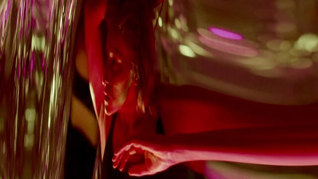Young woman giving emotionally intense dance performance in front of distorting mirror under vibrant multicolored neon light