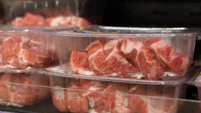 Refrigerated supermarket shelf displaying neatly stacked fresh pork cuts in plastic packaging, representing organized meat product selection ready for consumer purchase