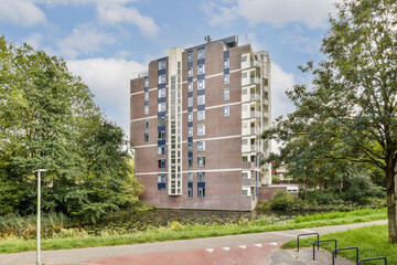 A stylish modern residential building stands beside a serene waterway, encircled by lush greenery...