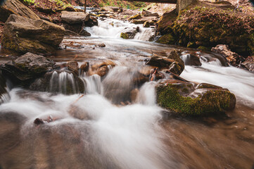 Obraz premium Serene mountain stream flowing over mossy rocks in a long exposure shot. Captures the tranquil beauty of nature with silky smooth water motion and earthy tones