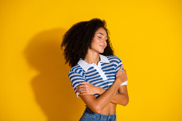 Beautiful young woman with curly hair smiling confidently against a vibrant yellow background,...