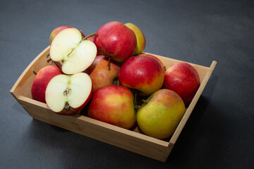 Fresh small organic red apples in a wooden crate on grey table background