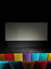 Empty cinema hall featuring a blank projection screen and a front row of vibrantly colored seats in...
