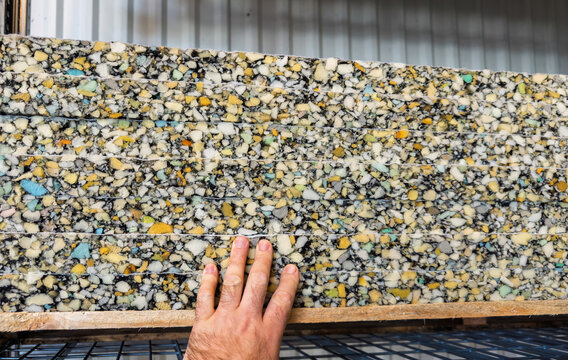 Close-up of a hand touching colorful recycled foam insulation sheets made from compressed polyurethane fragments, stacked horizontally on a metal shelf in a DIY store.