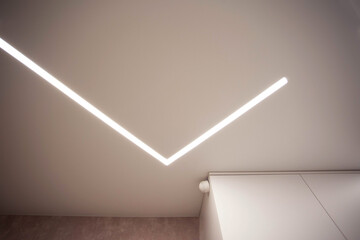 Modern designer stretch ceiling with illuminated LED lines in the room, backlighting