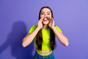 Smiling young woman in neon top gesturing enthusiastically against purple background, portraying...