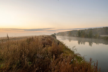 Morning fog on the lake at dawn. Colourful glow in the sky, with surrounding forest trees reflected in the calm water, in an atmospheric landscape.