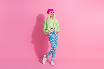 Young fashionable woman in casual attire posing against a vibrant pink background, showcasing trendy style with striped pants