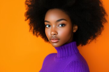 Portrait of Black woman with afro hairstyle wearing purple sweater on orange background, exuding poise and elegance through direct gaze and serene expression