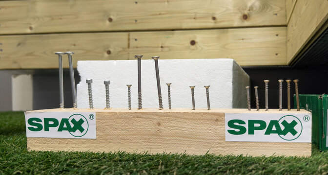 Paris, France - Mar 27, 2025: Display block featuring various SPAX screws of different lengths and head types inserted into wood, set on artificial grass with wooden paneling in the background.