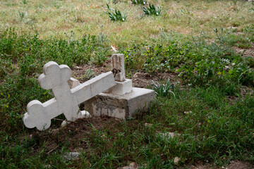 Fallen cross lying on grass symbolizing loss and grief. Ruined orthodox cemetery