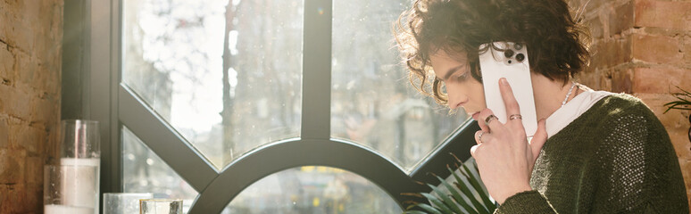 Young man enjoying a relaxed moment at a cafe while talking on the phone in the afternoon light
